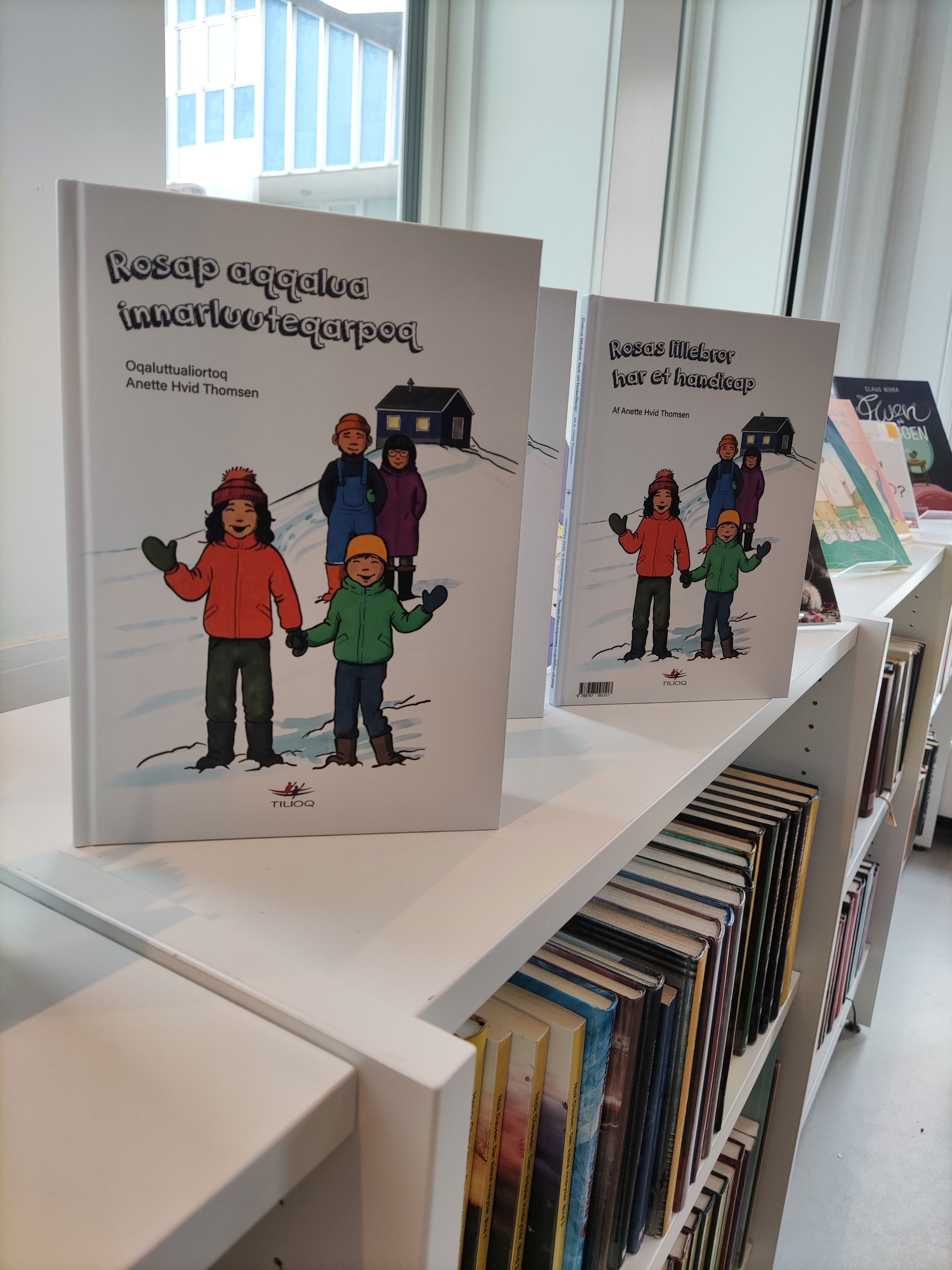 Bogen Rosas bror har et handicap på et bogreol, kopi på dansk og på grønlandsk.
