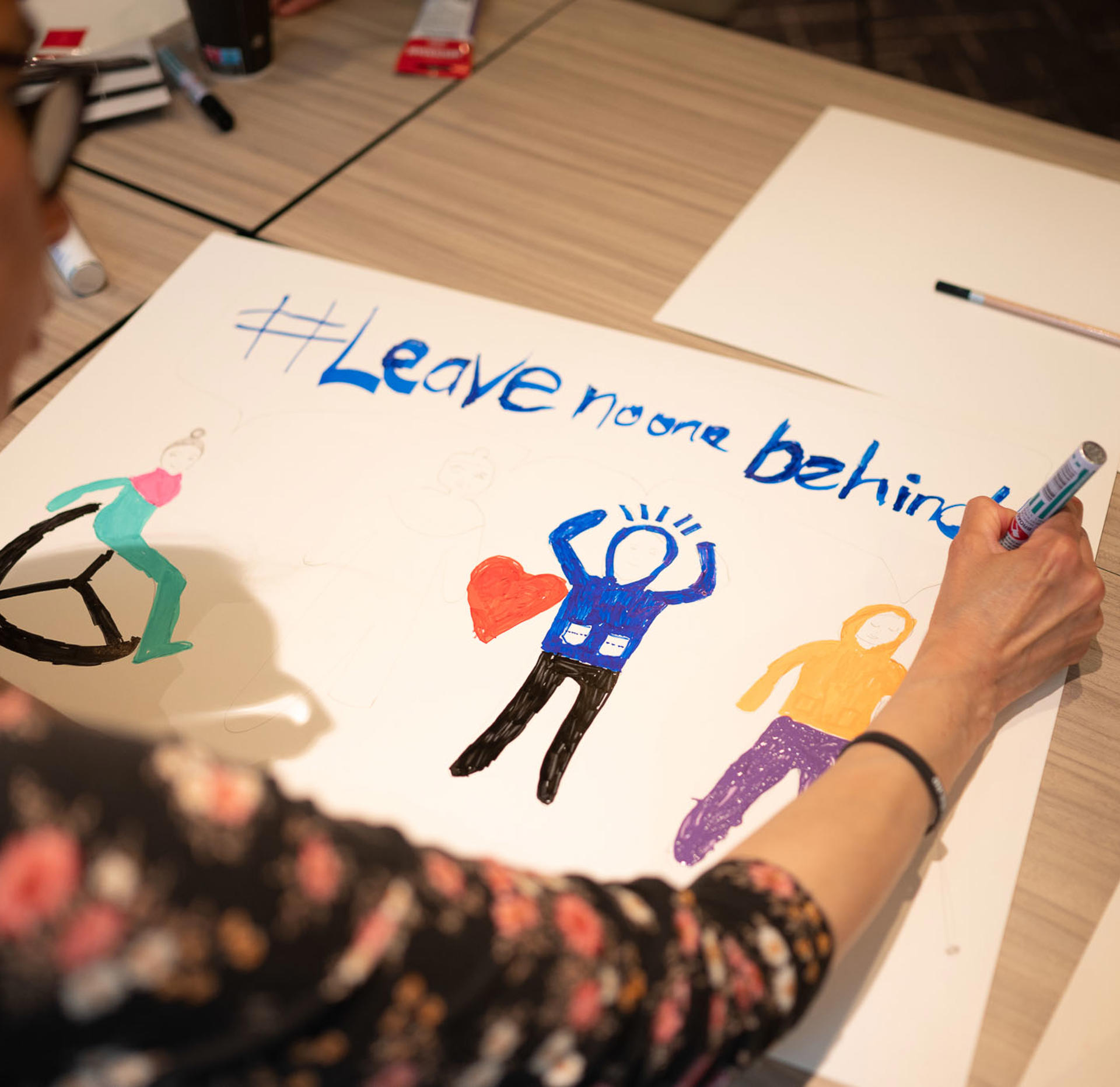 En ung kvinde der er i gang med at lave et skilt til Disability Pride. På den står der "Leave noone behind".